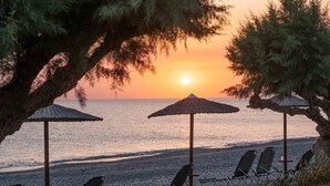 Une plage avec des chaises longues et des parasols en chaume, offrant une vue sur la mer au coucher du soleil.