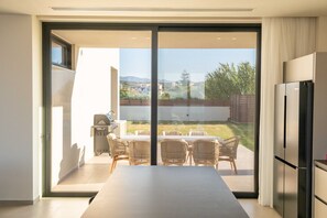 A modern kitchen with a large sliding glass door leading to an outdoor patio area. - Gemini Villas Chania | Complex of 2 villas (Maleme)