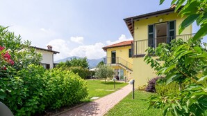 Ein gelbes Gebäude mit Balkon, umgeben von üppigem Grün und einem Ziegelweg.