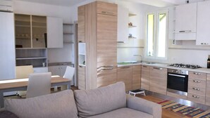 Eine moderne Küche mit weißen Schränken, ein Essbereich mit Tisch und Stühlen sowie ein Wohnzimmer mit einer Couch.