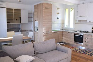 Eine moderne Küche mit weißen Schränken, ein Essbereich mit Tisch und Stühlen sowie ein Wohnzimmer mit einer Couch.