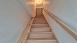 Una escalera de madera con barandilla, que lleva a una puerta en la parte superior.