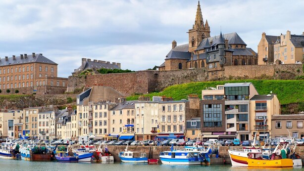 Un puerto con barcos amarrados, un edificio histórico con una torre y un muro de piedra.