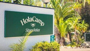 Un letrero verde con el texto 'HolaCamp Sitges Relax' y un símbolo de camping.