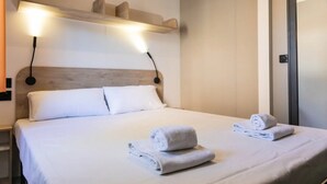 Una cama bien hecha con dos toallas enrolladas, un cabecero de madera y dos luces fijadas a la pared.