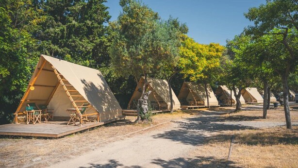 Una hilera de tiendas triangulares con terrazas de madera y asientos, rodeadas de árboles.