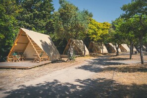 A row of triangular tents with wooden decks and seating, surrounded by trees. - Bungalow in Sitges, Barcelona for 4-people (Sitges, Barcelona)