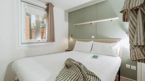 A neatly made bed with a striped blanket, a bedside lamp, and a window with curtains.
