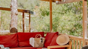 A wooden deck with a red sofa, a wicker basket, and a straw hat.
