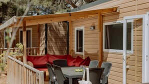 Eine Holzhütte mit überdachter Veranda, auf der ein Tisch und Stühle sowie eine rote gepolsterte Bank und ein kleines Fenster zu sehen sind.
