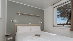 Ein ordentlich gemachtes Bett mit weißen Leinen, ein Buch auf dem Bett und ein Fenster mit Blick auf Bäume.