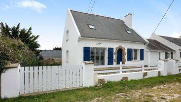 A white house with blue shutters, a white picket fence, and a clear sky.