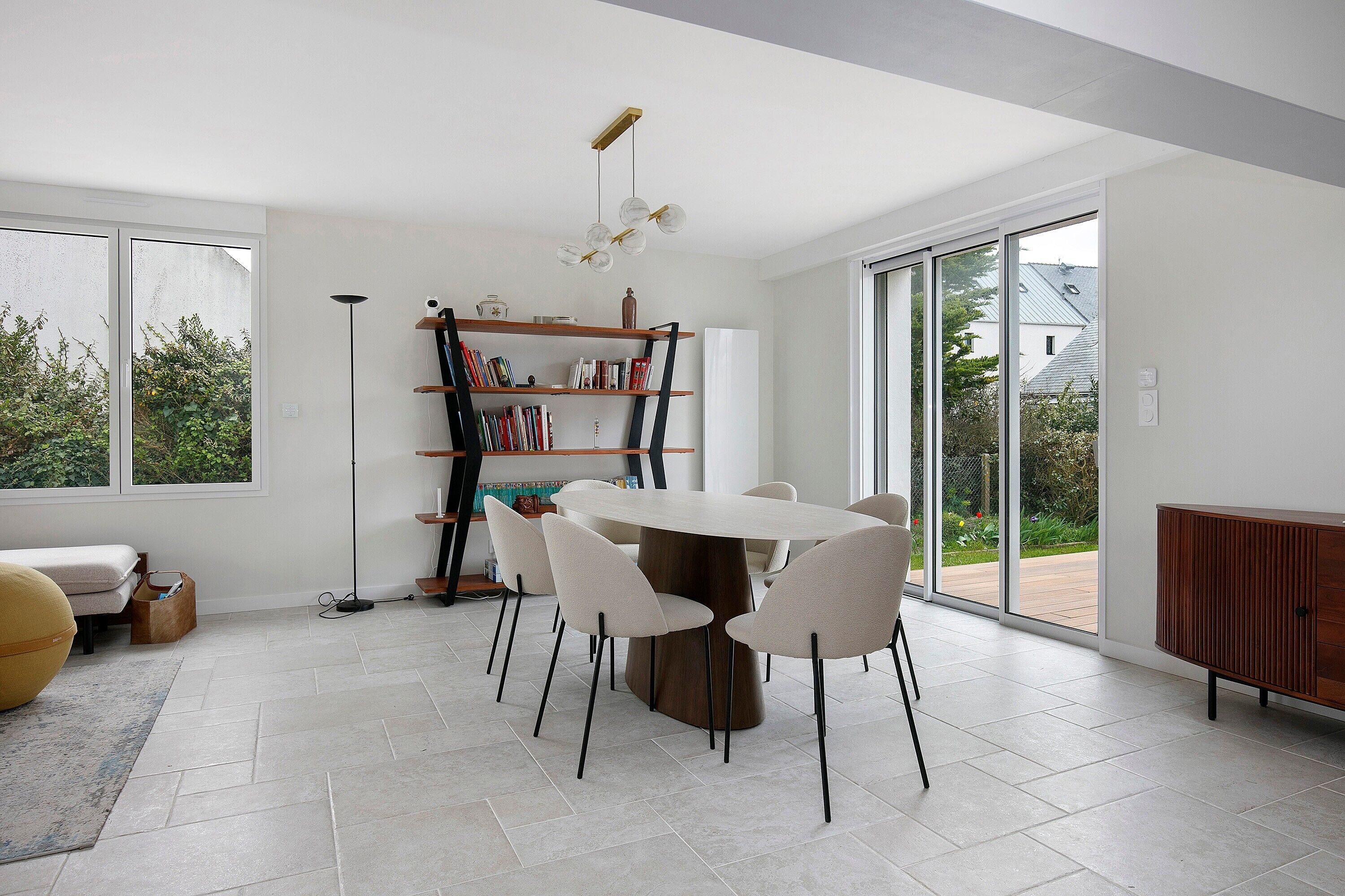 Un espace repas moderne avec une table ronde, des chaises blanches, une bibliothèque et une vue dégagée grâce à de grandes fenêtres.
