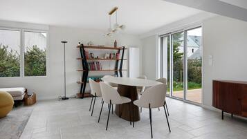 Un espace repas moderne avec une table ronde, des chaises blanches, une bibliothèque et une vue dégagée grâce à de grandes fenêtres.