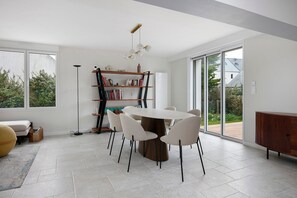 Un espace repas moderne avec une table ronde, des chaises blanches, une bibliothèque et une vue dégagée grâce à de grandes fenêtres.