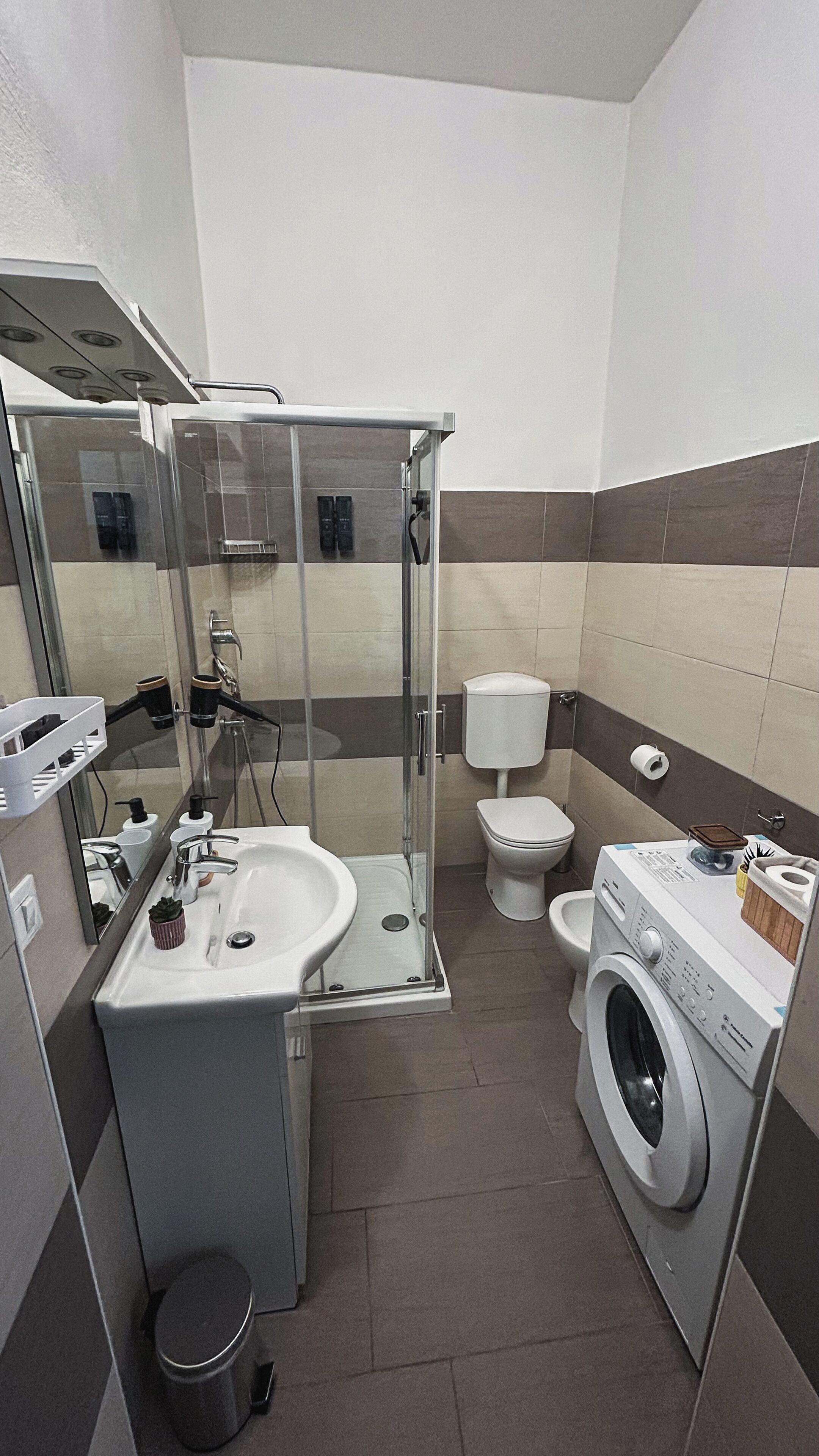 Ein kleines Badezimmer mit Waschbecken, Spiegel, Toilette und Waschmaschine.