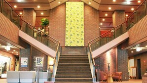 A staircase in a lobby with a brick wall and a large vertical banner. - Arima Onsen Maple Arima (Kobe)