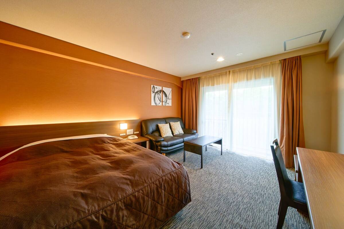 A hotel room with a large bed, a sofa, a small table, and a desk.