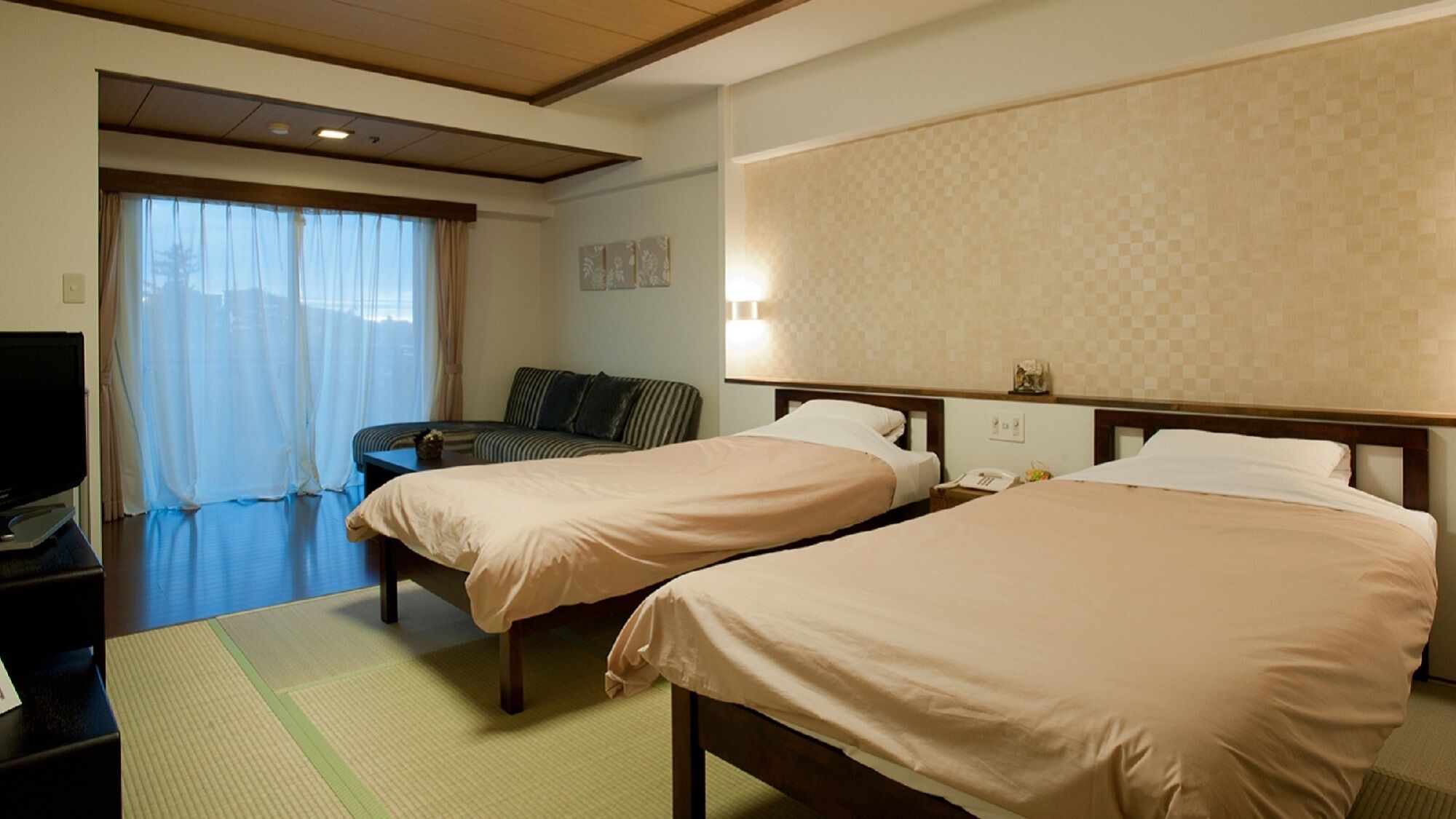 A hotel room with two beds, a television, a sofa, and a window with curtains.