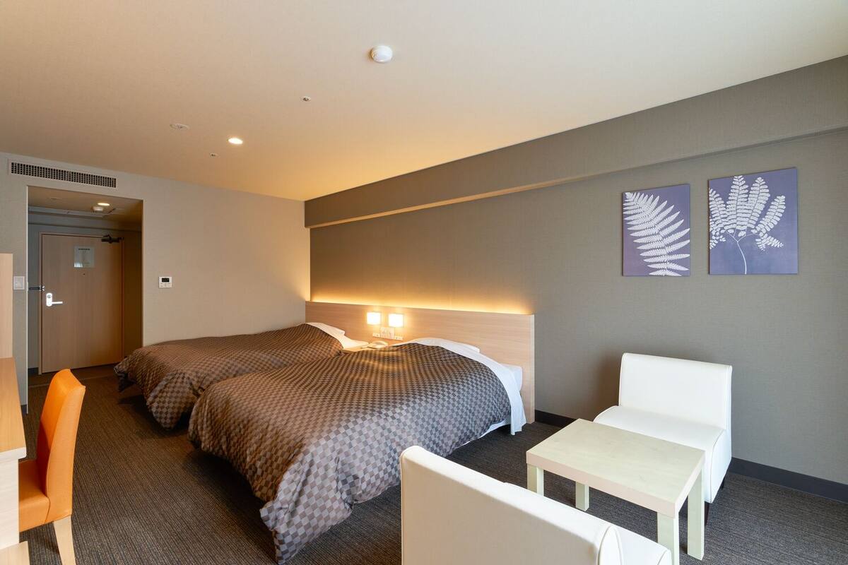 A hotel room with two beds, a desk, a chair, and artwork on the wall.