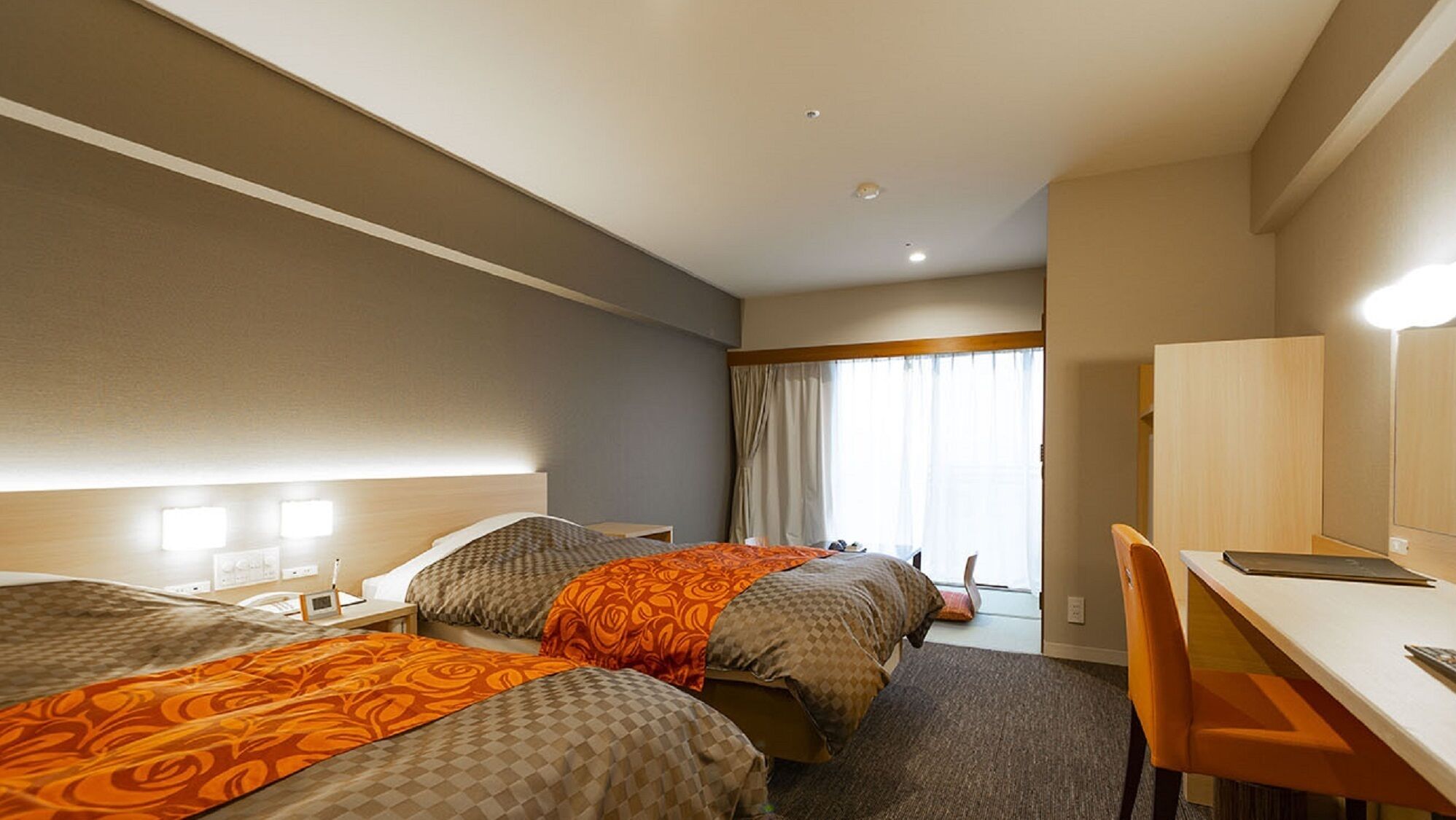 A hotel room with two beds, a desk, a chair, and a large window with curtains.