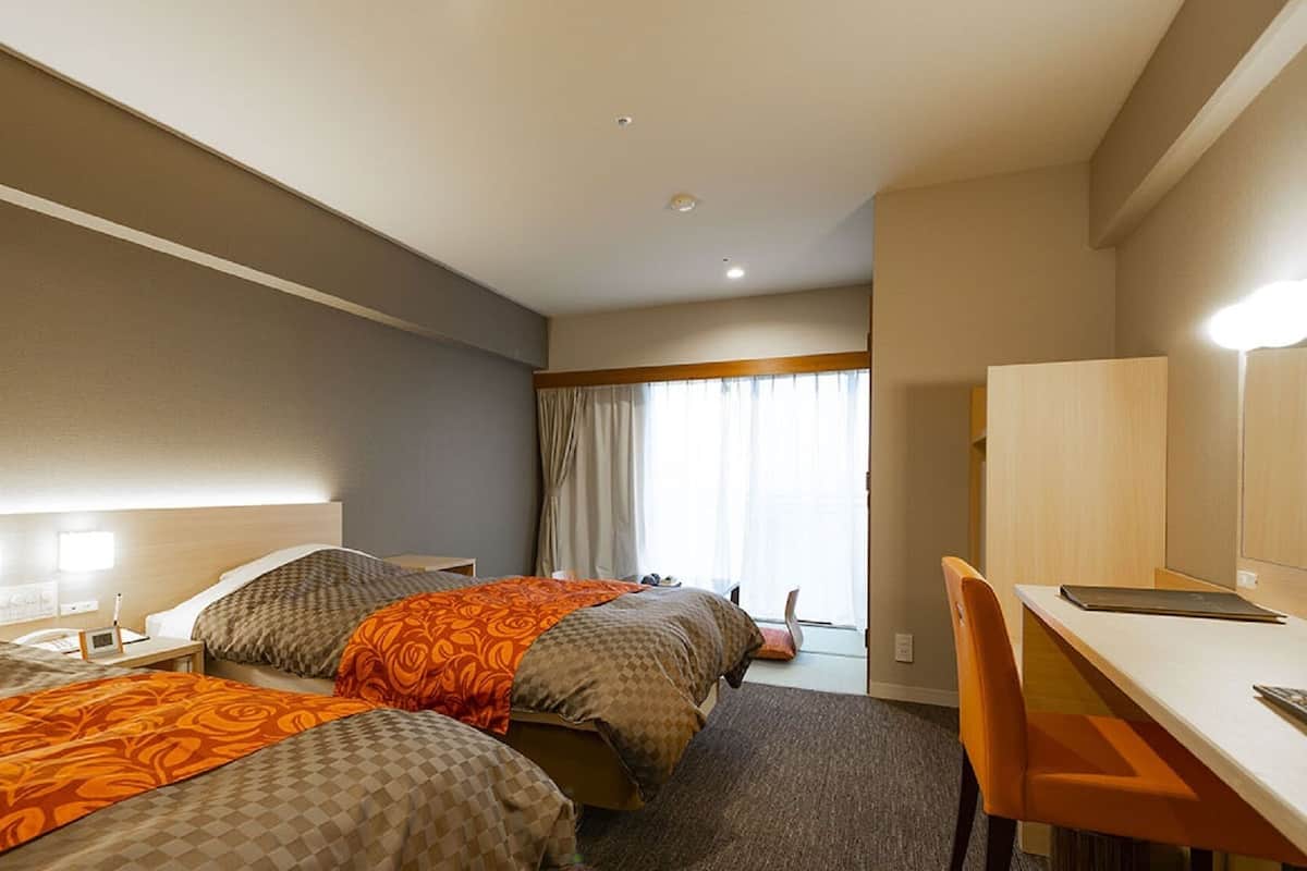 A hotel room with two beds, a desk, a chair, and a large window with curtains.
