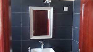 Une salle de bain avec un mur recouvert de carreaux foncés, un lavabo blanc avec un miroir au-dessus, et une porte en bois.