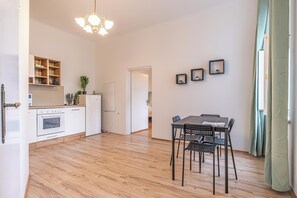 Une cuisine moderne avec des meubles blancs et un four encastré, un coin repas avec une table et des chaises, et un couloir menant à une autre pièce.