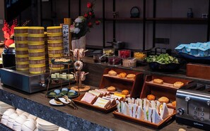 A buffet with various food items, including pastries, sandwiches, and a drink station.