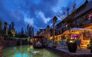 A serene evening pool area with a wooden deck, lounge chairs, and a small boat.