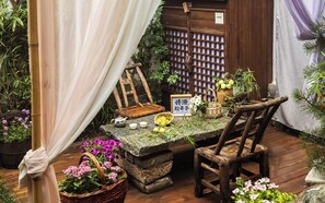 A rustic outdoor seating area with a stone table, wooden chairs, and various plants.