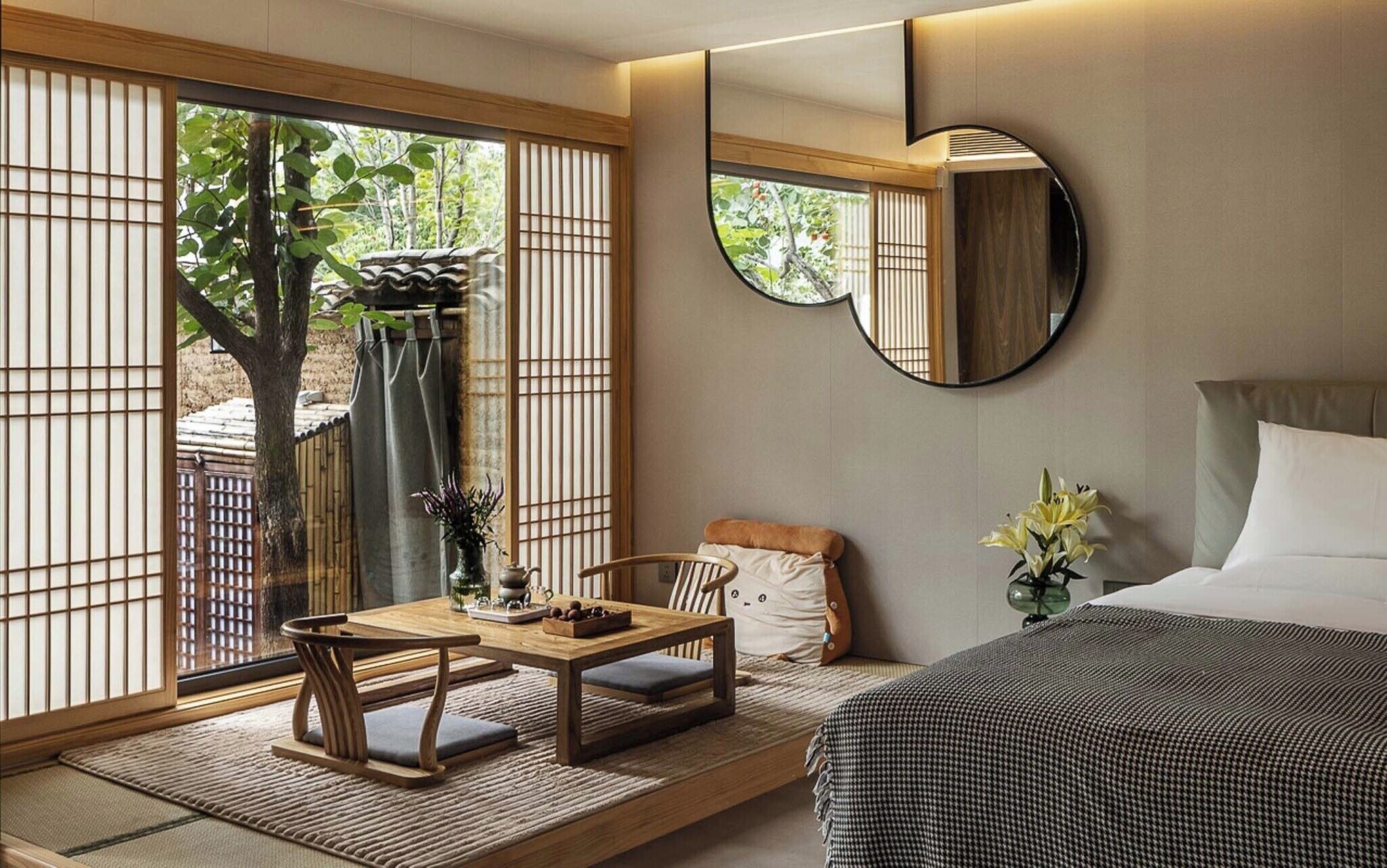 Une pièce de style japonais traditionnel, avec un sol recouvert de tatamis, une table basse, une chaise, un lit et une grande fenêtre dotée de stores en bambou.
