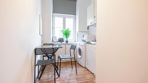 A compact kitchen with a washing machine, a small table with chairs, and a window with a plant. - Charming 1BR Near Prater and Danube (Vienna)