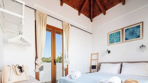 A bedroom with a bed, towels, a hat, a hanging rack, and a view of the outdoors. - Villa Aliki – Sea Views & Just 750m from the Beach (Rethymno)
