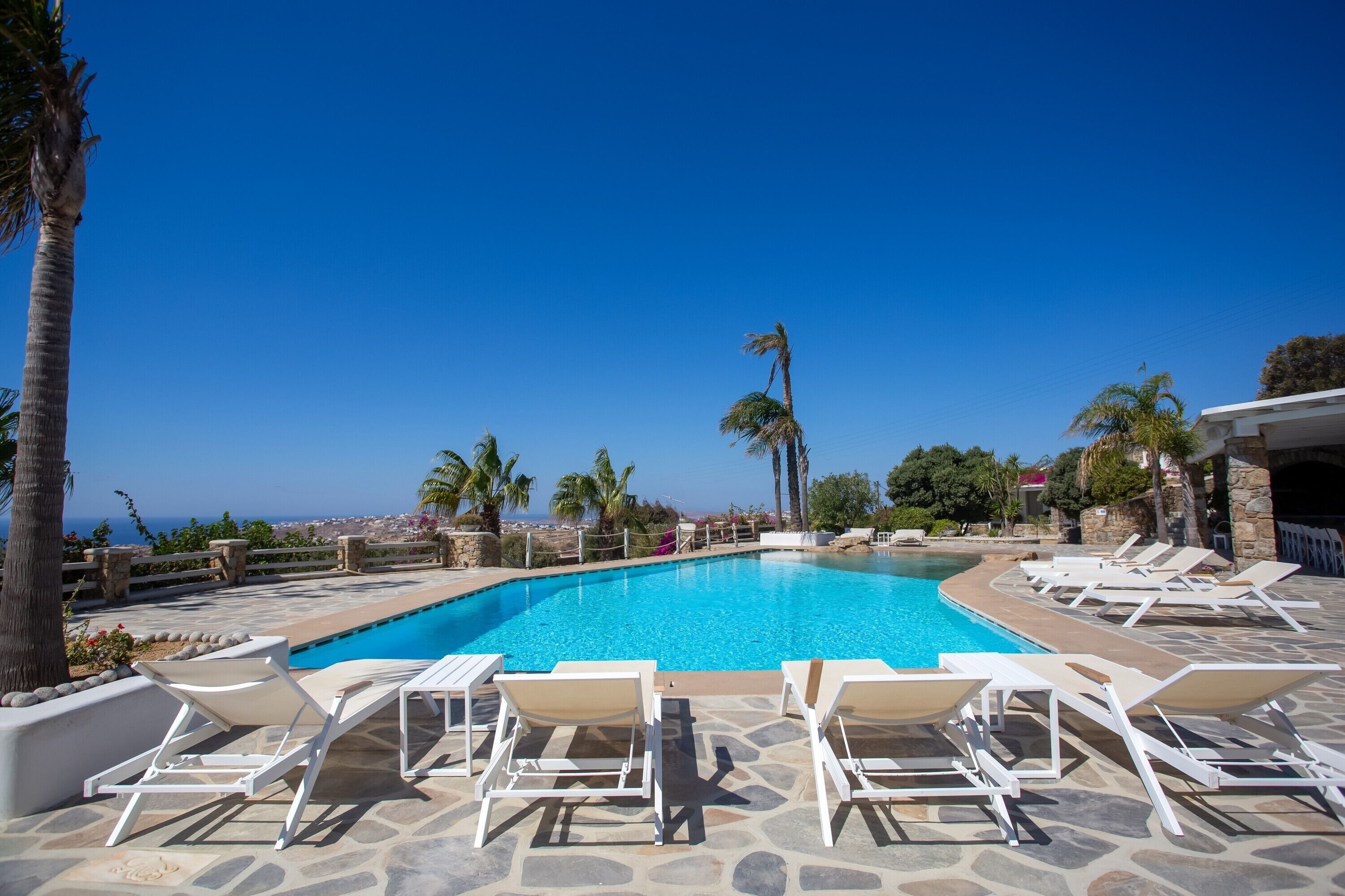 A swimming pool with lounge chairs, palm trees, and a view of the sea.