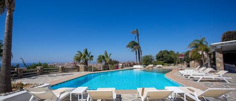 A swimming pool with lounge chairs, palm trees, and a view of the sea.