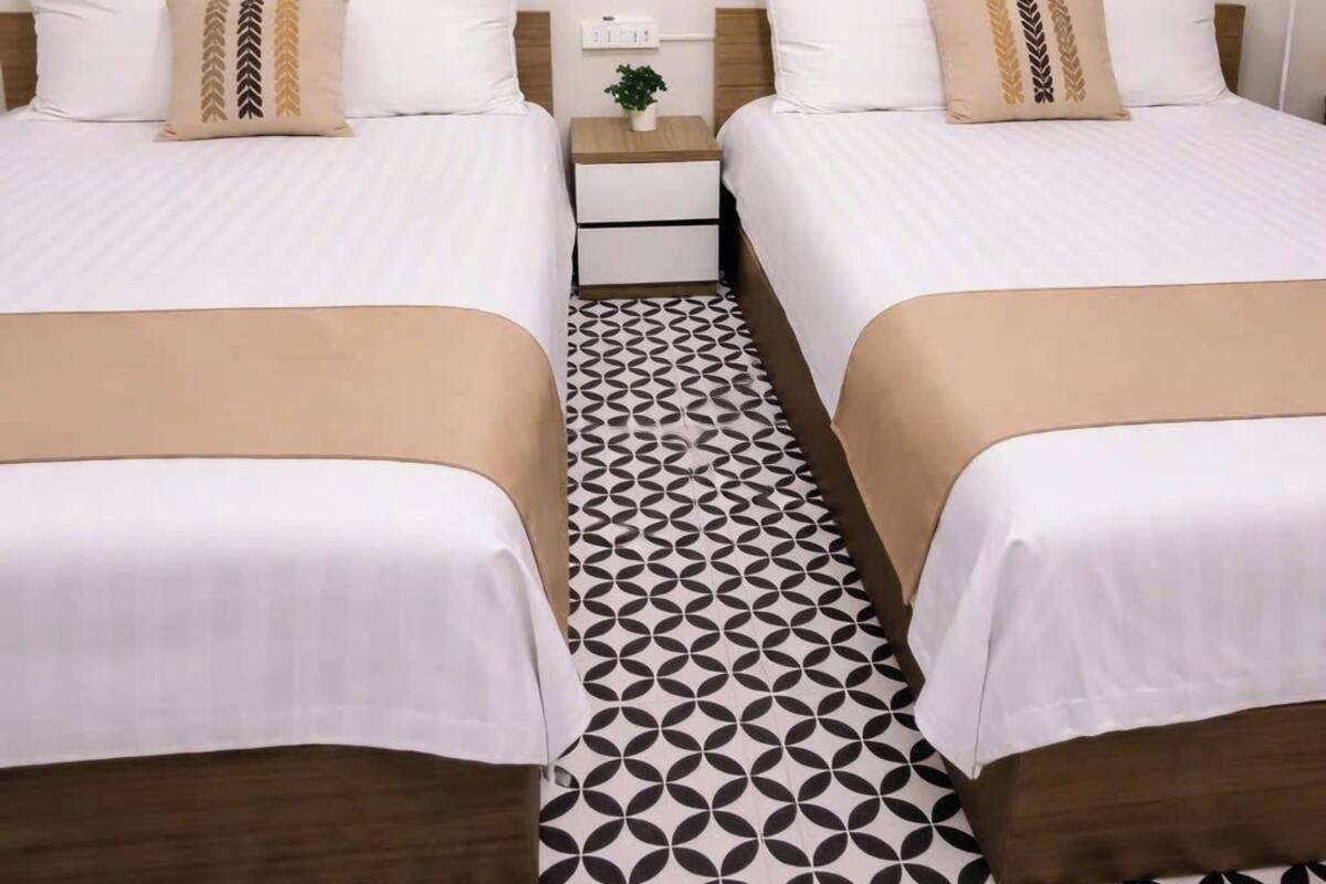 A hotel room with two beds, a nightstand, a painting on the wall, and a patterned floor.