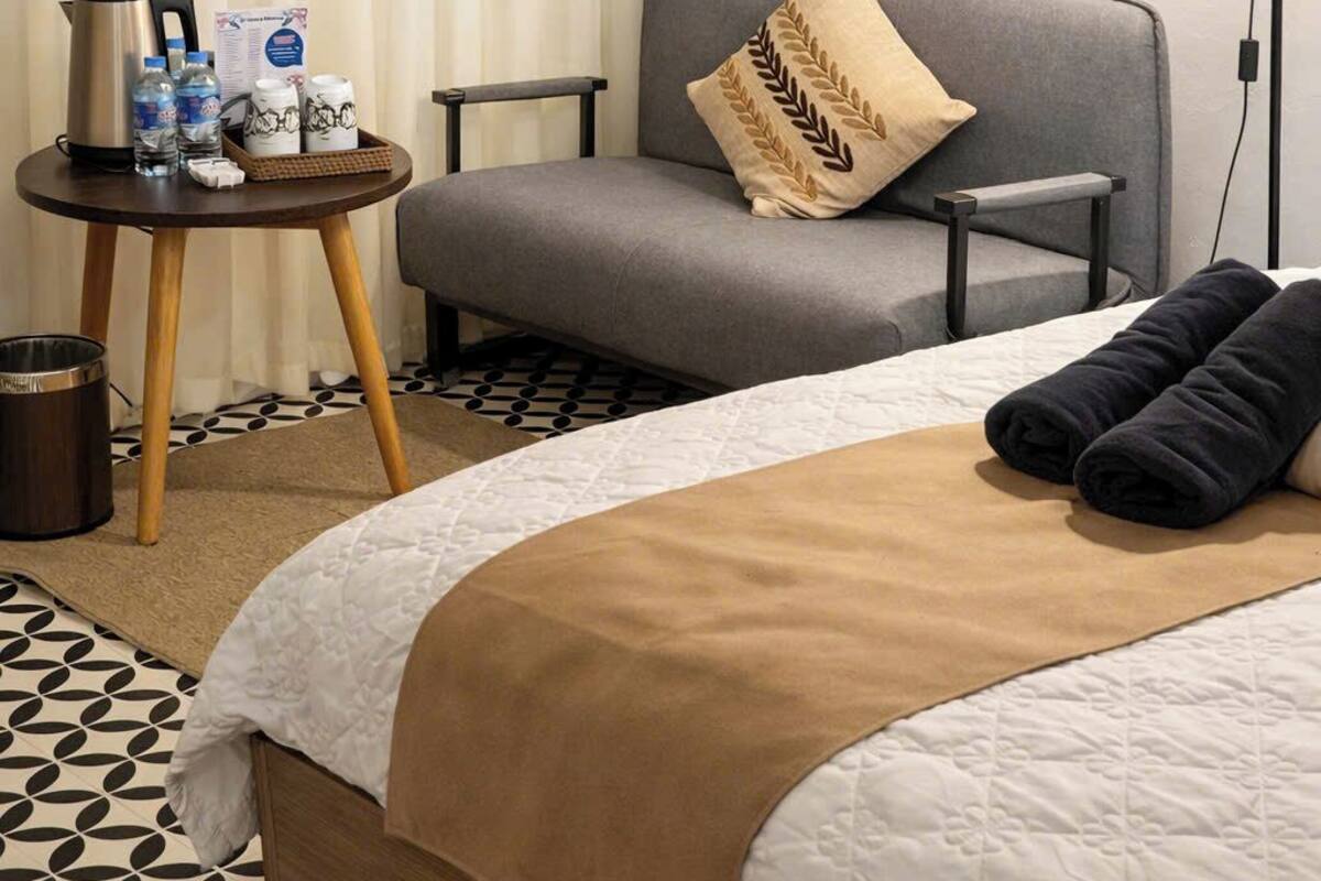 A hotel room with a bed, a sofa, a small table with amenities, a lamp, and a painting on the wall.