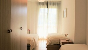 Ein Hotelzimmer mit zwei Betten, einem Fenster mit Vorhängen, einem Nachttisch mit Lampe und einer Tür.