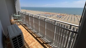 Ein Balkon mit Blick auf einen Strand mit Reihen von Sonnenschirmen und Liegestühlen.