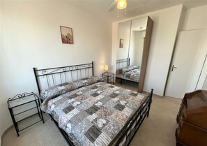 A bedroom with a bed, a bedside table, a mirror, and a wardrobe. - Apartment with sea view in Lignano (Lignano Sabbiadoro)
