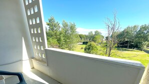 En balkon med udsigt over en grøn græsplæne og træer.