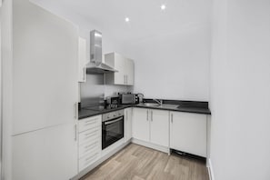 A modern kitchen with white cabinets, a built-in oven, a microwave, and a sink. - Guestready - Gladstone (Liverpool)
