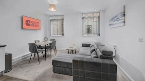 Un salon moderne avec un coin repas, des canapés gris, une petite table et un panneau indiquant « PRÊT POUR LES INVITÉS ».