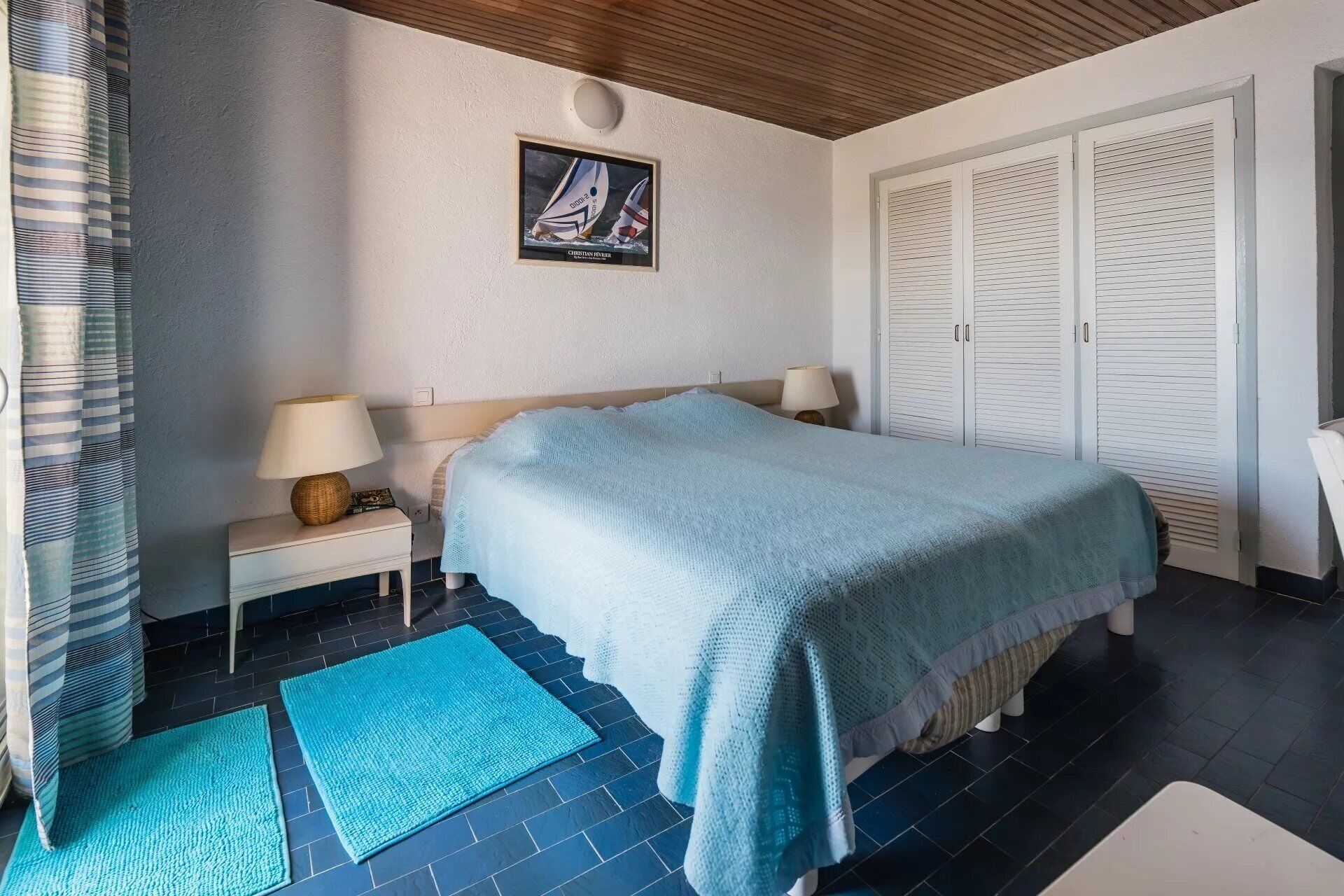 A bedroom with a bed, nightstands, a lamp, a framed picture, and a wardrobe.