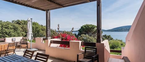 An outdoor patio with a table and chairs, a pergola, and a view of a lake and hills.