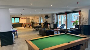 Een pooltafel in een goed verlichte kamer met een eethoek, banken en een kerstboom.