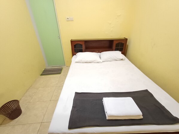 A single-bed room with a wooden headboard, white bedding, and a black blanket folded on the bed.