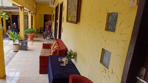 A yellow-walled indoor area with a red sofa, a table with a vase, and potted plants. - Irma Guest House (Malang)