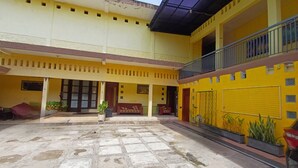A courtyard with a tiled floor, a red sofa, and a potted plant. - Irma Guest House (Malang)